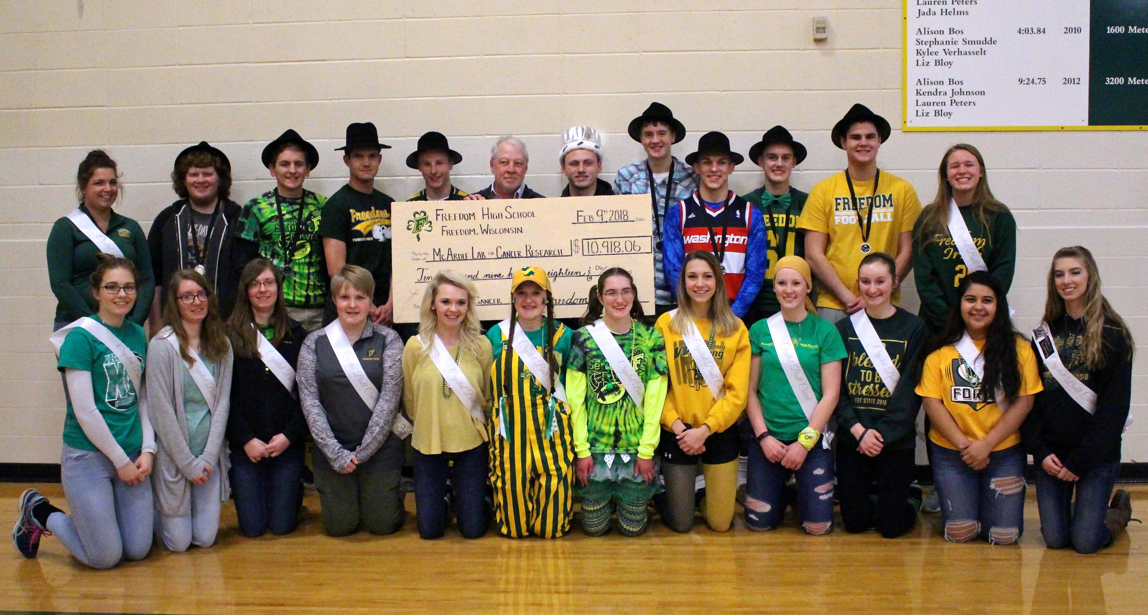 A group of highschool students  in a gym posing with a giant check
