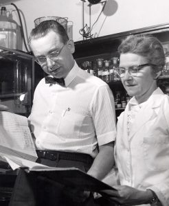 A man and a woman standing side by side reading a book